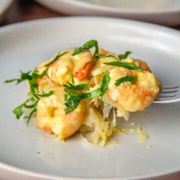 Dijon-sauced shrimp topped with fresh herbs sits on a bed of sauerkraut on a plate.