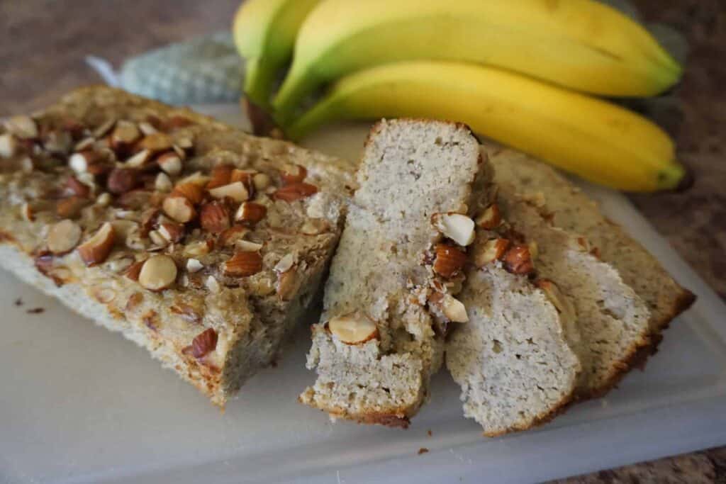 Keto banana bread loaf with slices on cutting board next to whole bananas.