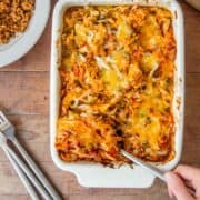 A white baking dish holds cheesy chicken casserole with a fork lifting a portion.
