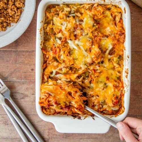 A white baking dish holds cheesy chicken casserole with a fork lifting a portion.