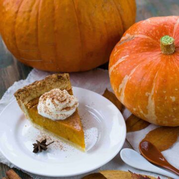dairy-free keto pumpkin pie with coconut whipped cream and pumpkins on a table
