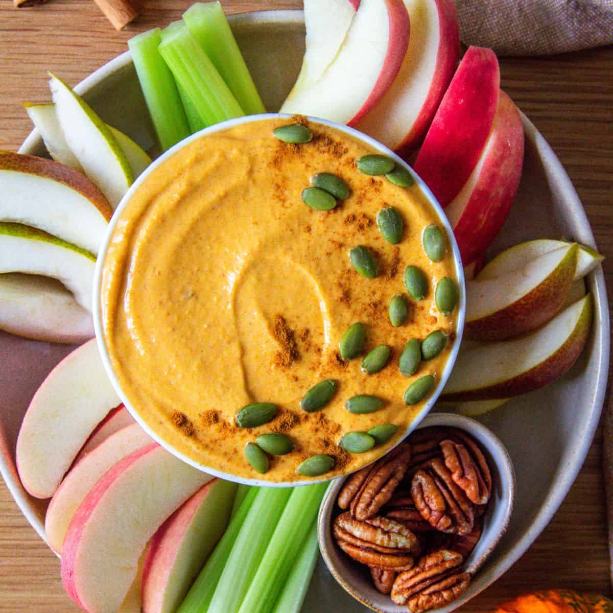 Healthy pumpkin pie dip served with apple slices, celery, and pecans.