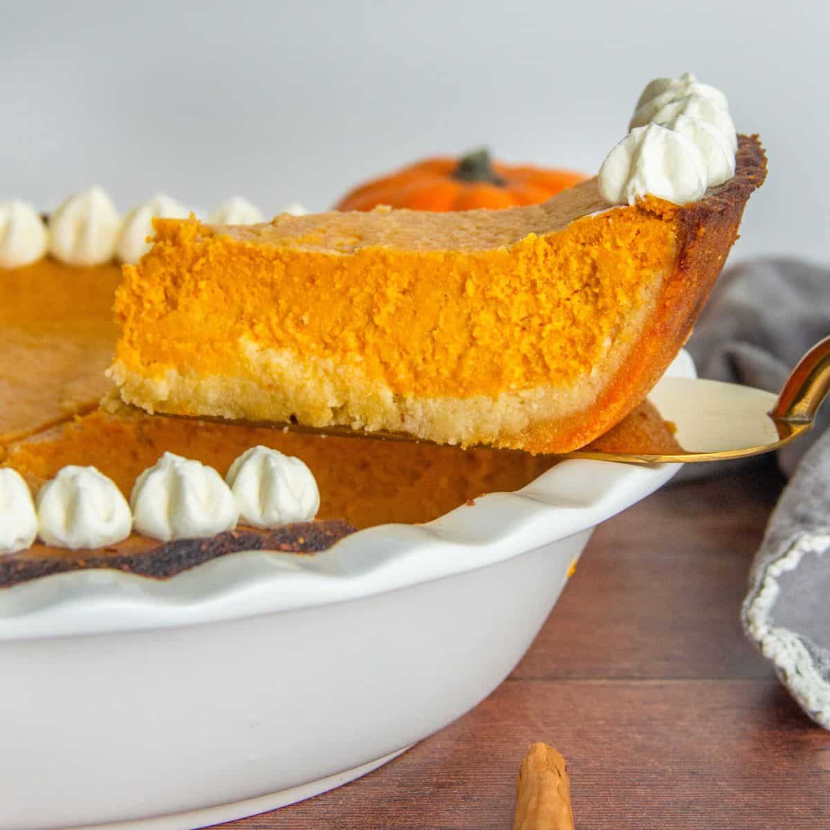 A slice of pumpkin pie topped with whipped cream and ready to be served on a plate.