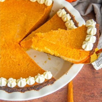 A slice of pumpkin pie topped with whipped cream and ready to be served on a plate.