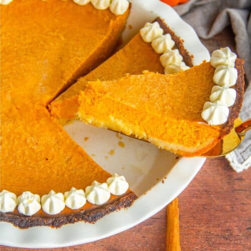 A slice of pumpkin pie topped with whipped cream and ready to be served on a plate.