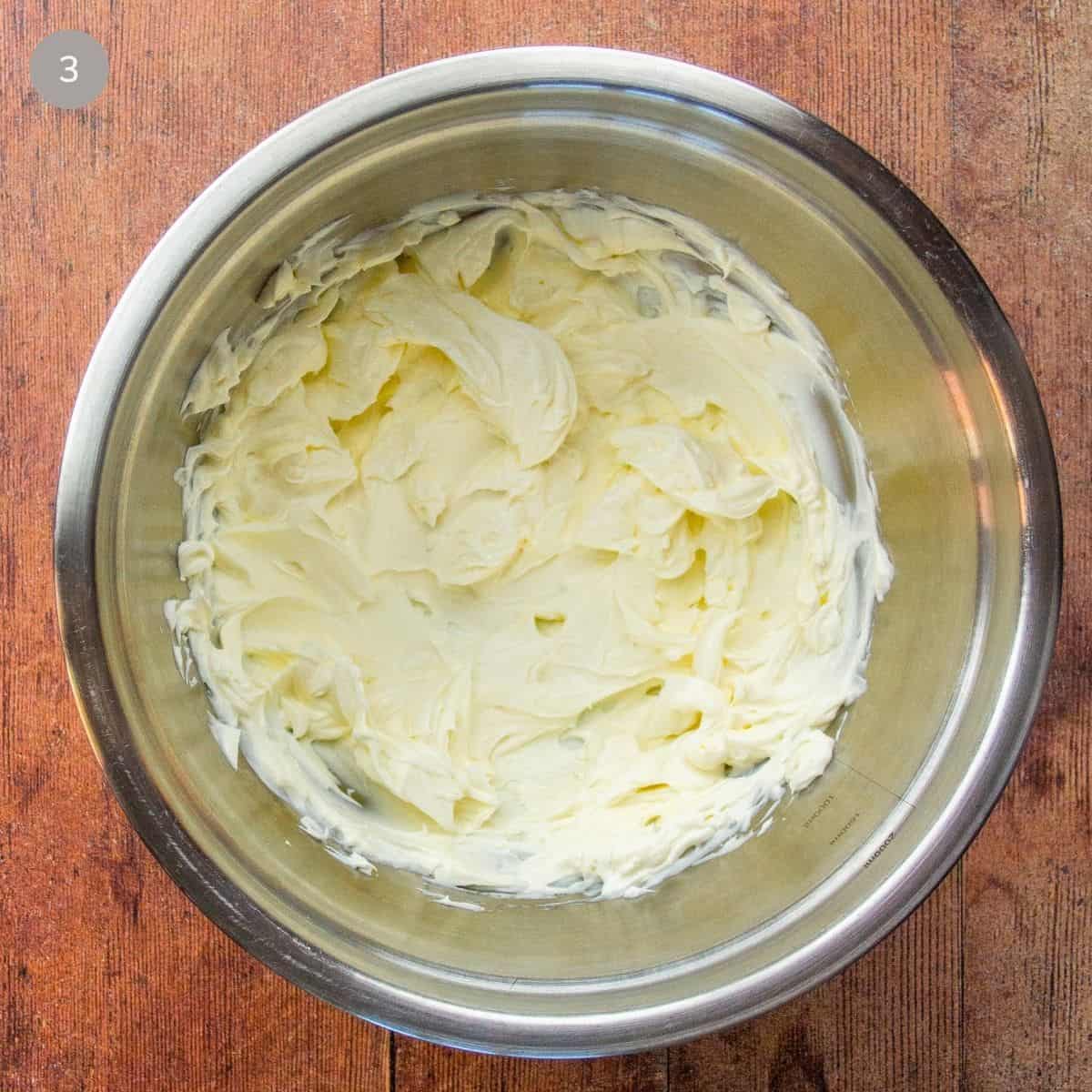 A bowl of cream cheese placed on a rustic wooden table, showcasing its creamy texture and rich color.