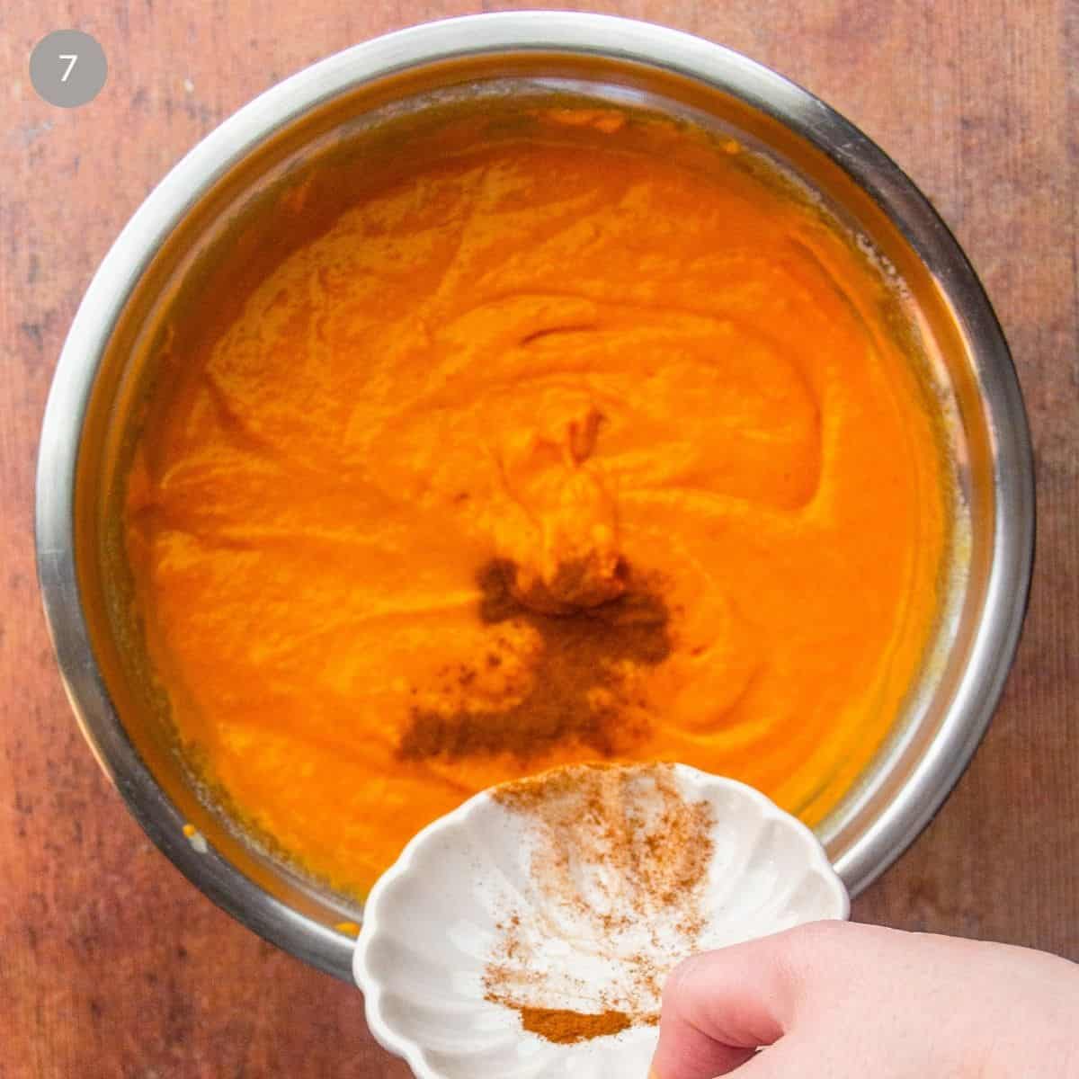A person adding the vanilla and cinnamon into the mixture in a metal bowl.