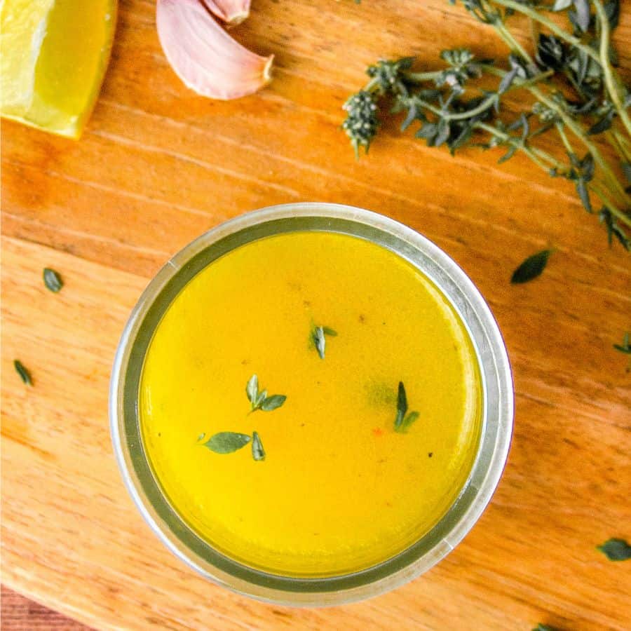 Lemon pepper vinaigrette in a jar, garnished with thyme, next to fresh thyme and garlic.
