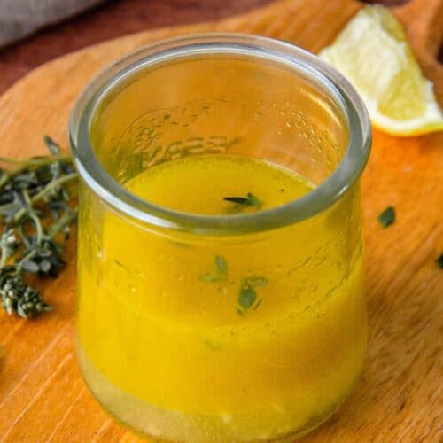 Lemon pepper vinaigrette in a glass jar with fresh thyme and a lemon wedge nearby.