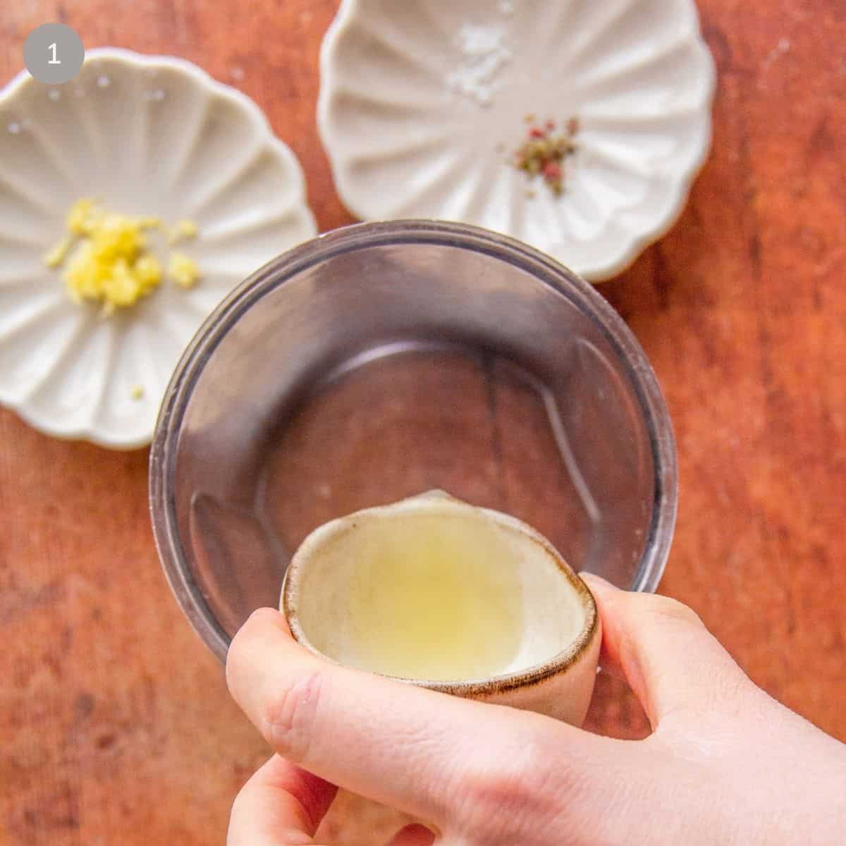 Lemon juice poured into a small blender cup with garlic and seasoning bowls nearby.
