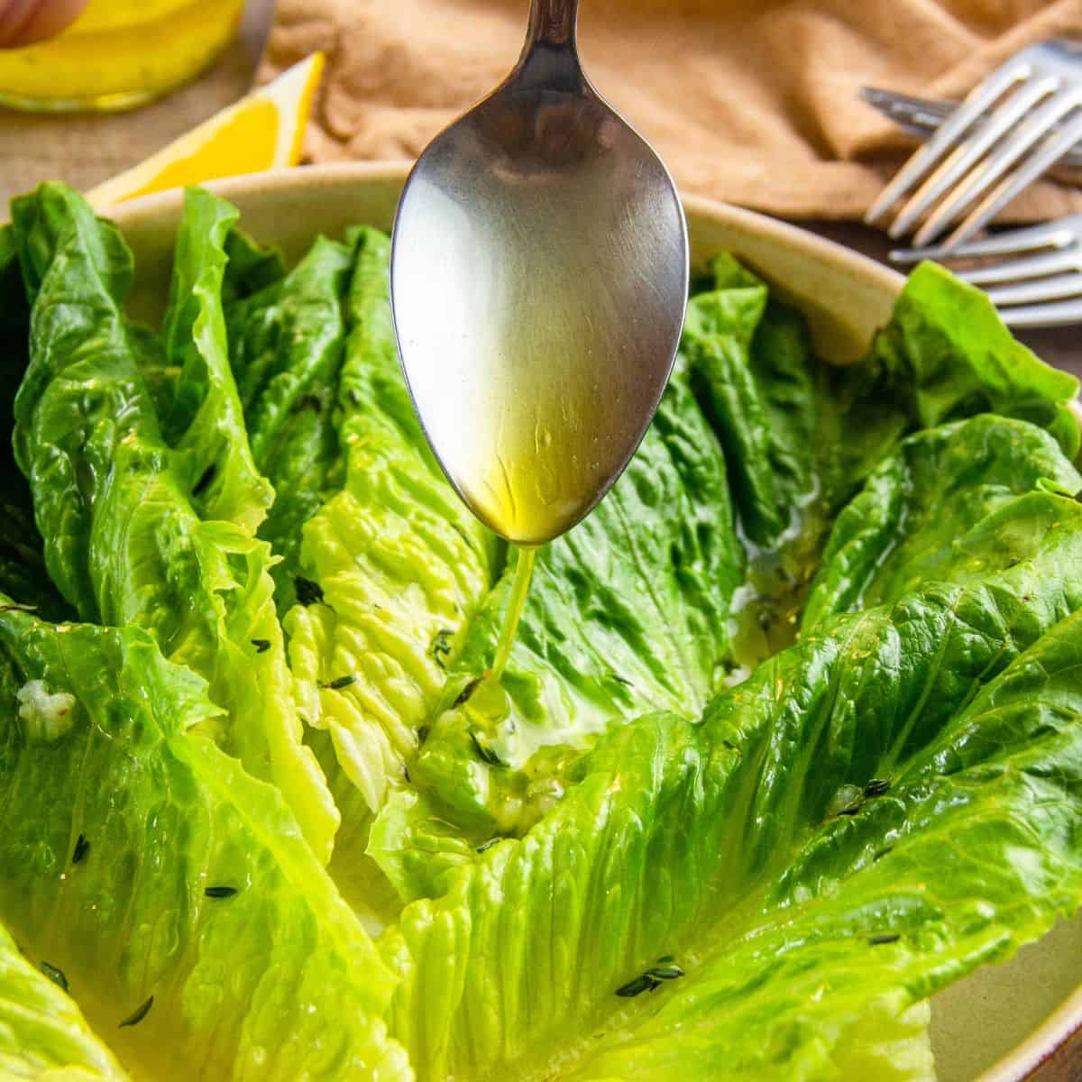 Spoon drizzling lemon pepper vinaigrette over romaine lettuce leaves in a bowl.