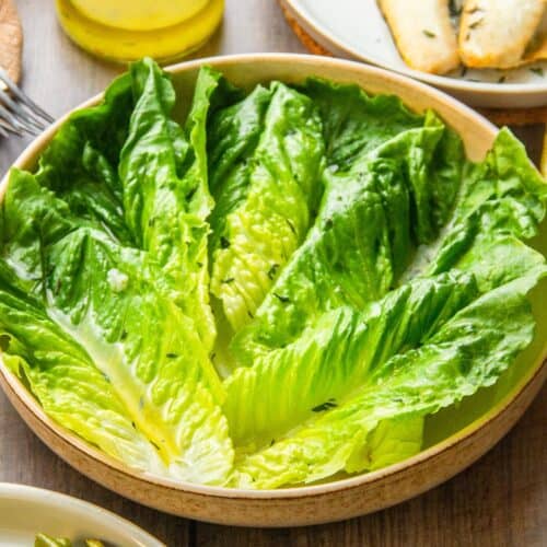 Romaine lettuce leaves dressed with lemon pepper vinaigrette, garnished with herbs, in a bowl.