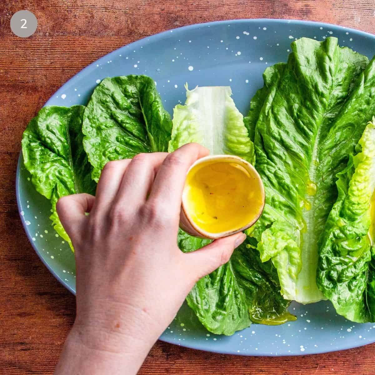 Pouring lemon pepper vinaigrette over romaine lettuce leaves on a plate.
