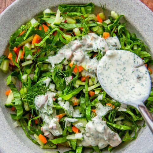 Shredded green salad with carrots and radish, drizzled with creamy bacon ranch dressing from a spoon.