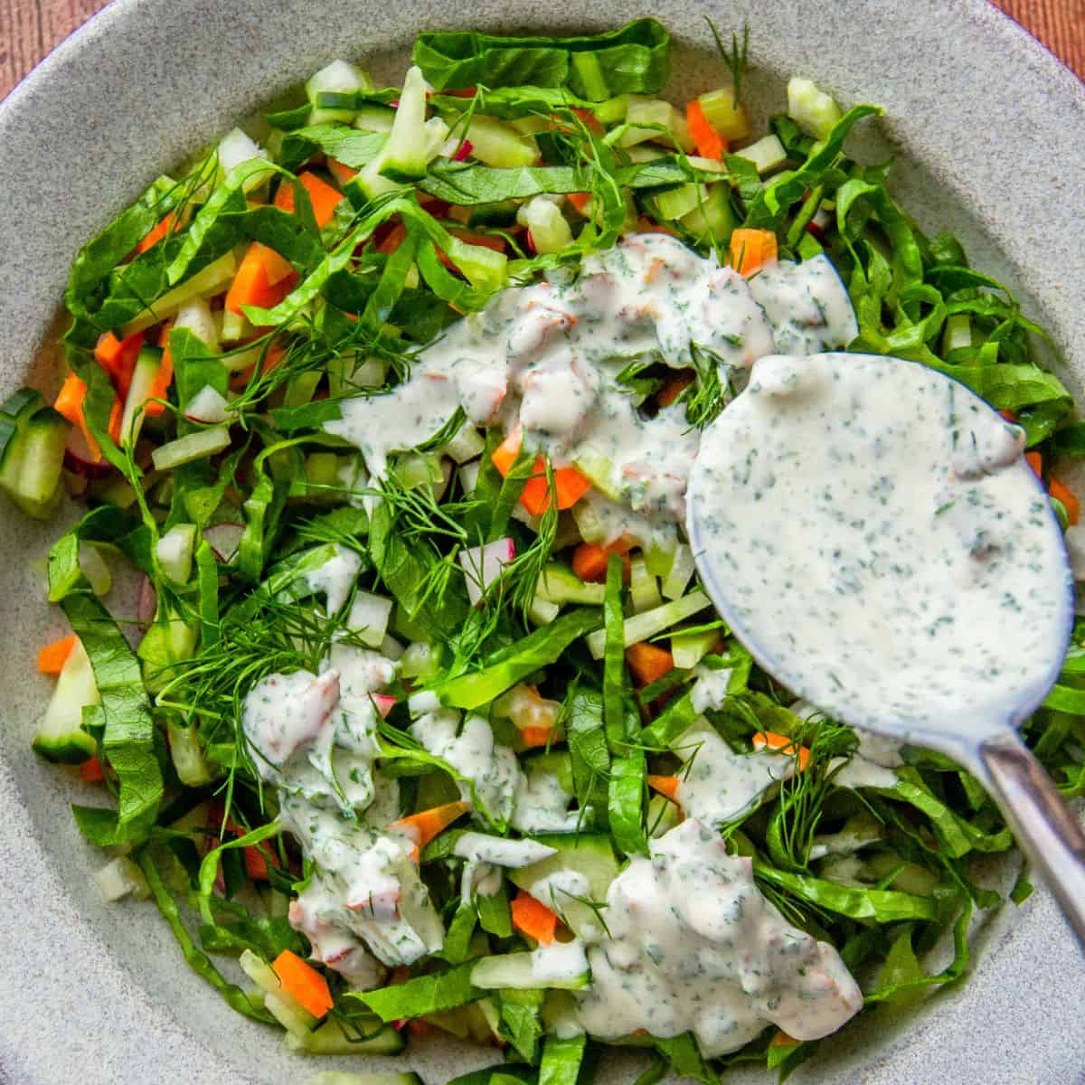 Shredded green salad with carrots and radish, drizzled with creamy bacon ranch dressing from a spoon.