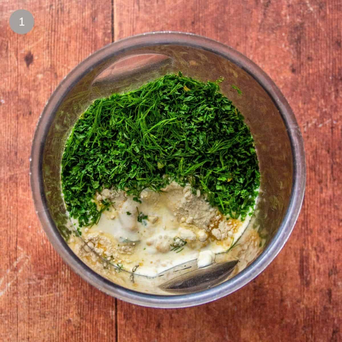 Chopped dill and parsley, cream, mayonnaise, and spices sitting unmixed in a metal bowl.