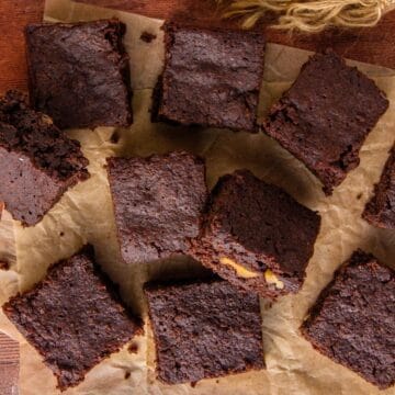 Cut chocolate brownies, some with visible walnuts, sit scattered on brown parchment paper.
