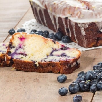 Slice of lemon blueberry cake, fresh blueberries, cake loaf in background.