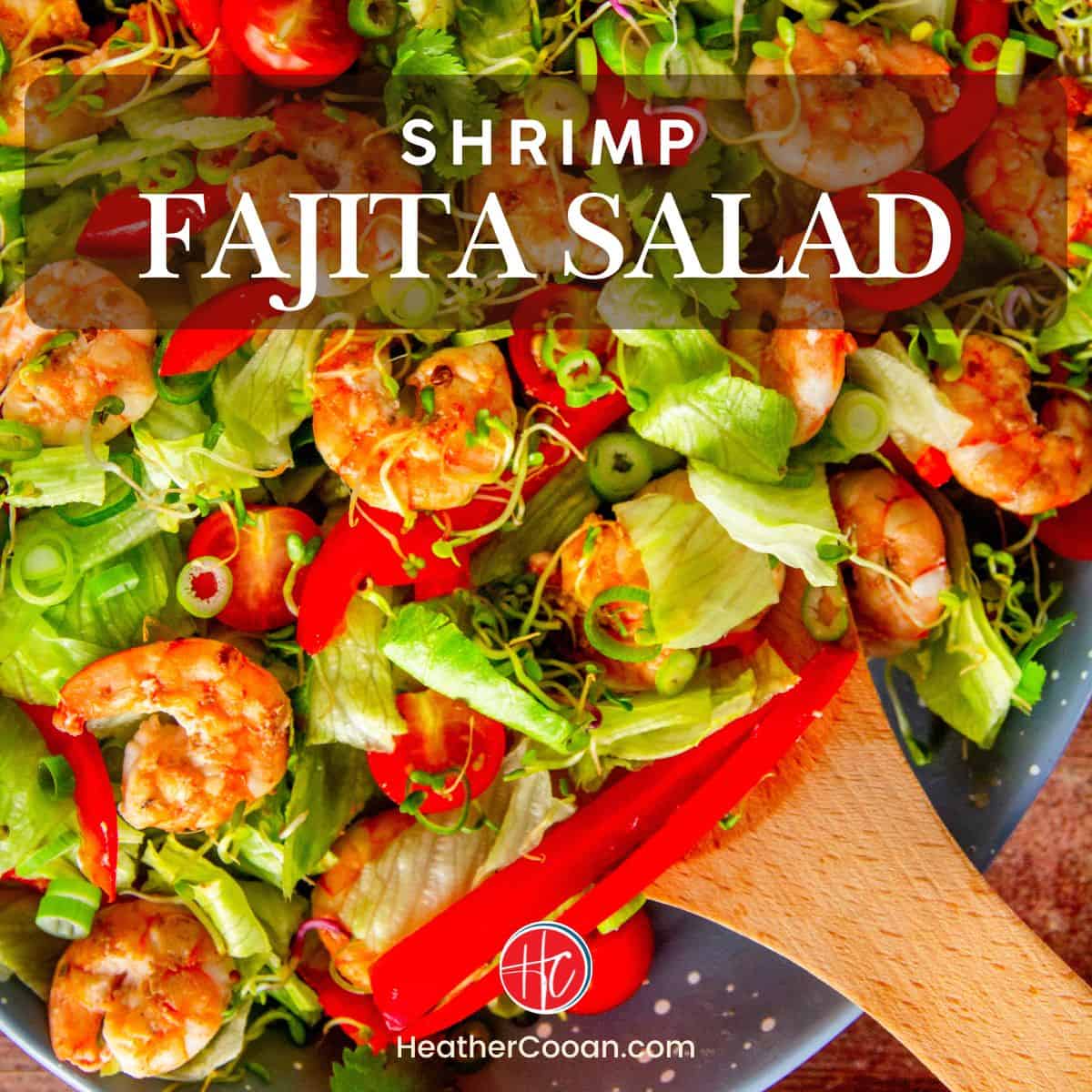 Close-up of shrimp salad with lettuce, red pepper, tomatoes, and sprouts, wooden spoon resting on top.