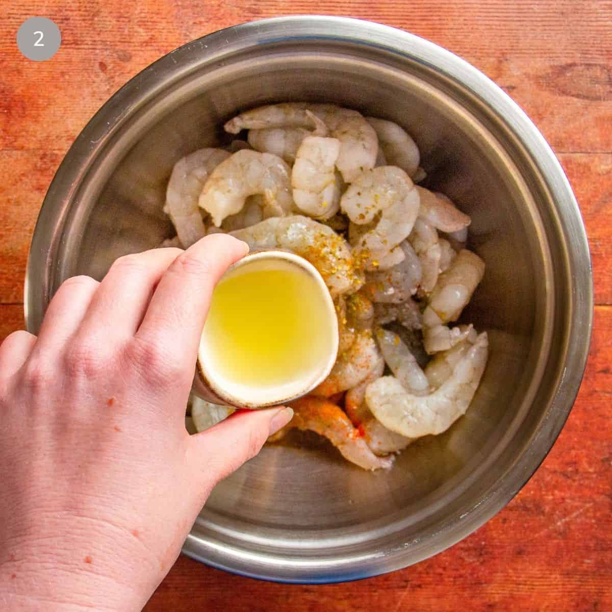 Hand pours lemon juice into a bowl of raw shrimp seasoned with spices.