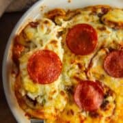 Close-up of melted mozzarella and pepperoni over baked chicken in a white dish.