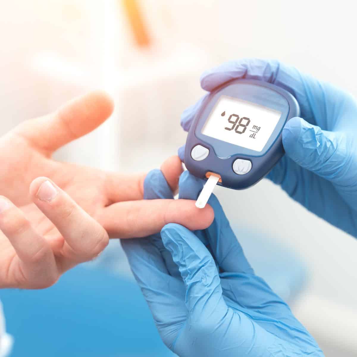 gloved hands using a blood glucose meter to check blood sugar