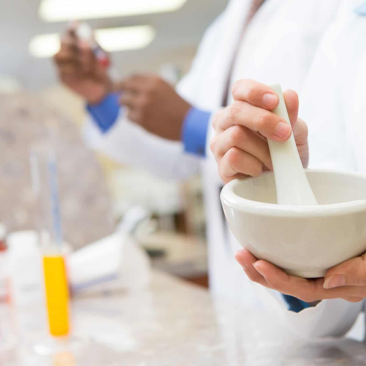 female compounding pharmacist holding mortar and pestle with male pharmacist in the background