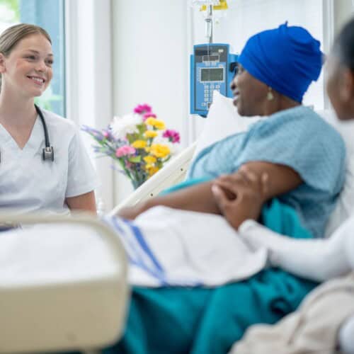 Woman receiving chemotherapy in hospital bed with doctor and family at bed side.