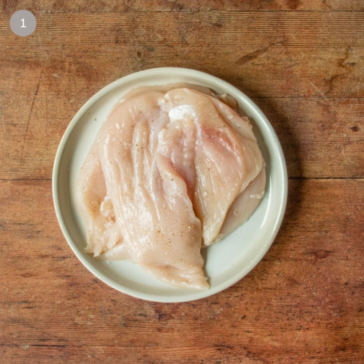 Raw chicken breasts seasoned with salt and pepper on a white plate, ready to sauté.