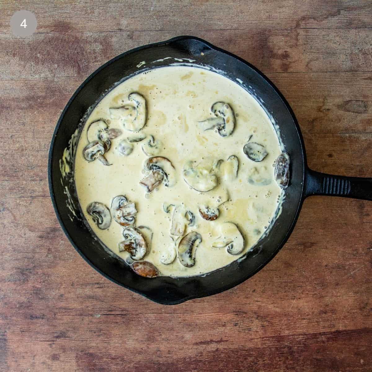 Mushrooms simmering in a creamy Dijon sauce in a cast iron skillet on a wood table.